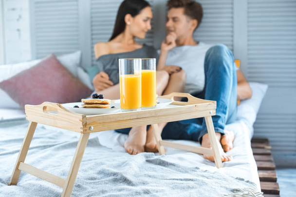 Selektivní fokus multikulturní pár a snídani na dřevěný tác na lůžku v ložnici - Fotografie, Obrázek