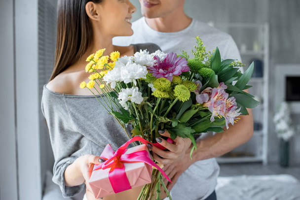 vue partielle de l'homme étreignant femme souriante avec présent et bouquet de fleurs à la maison
 - Photo, image
