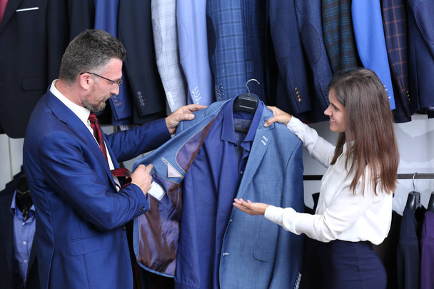 Young shop assistant helping man to choose suit in store - Fotó, kép