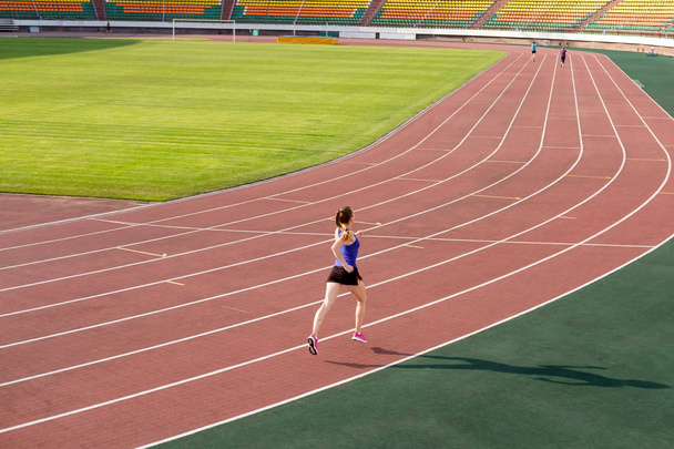 Deporte. Mujer joven atlética en zapatillas de deporte de color rosa corren en el estadio de atletismo. Concept run. Ejecutar la competencia en el estadio
. - Foto, imagen