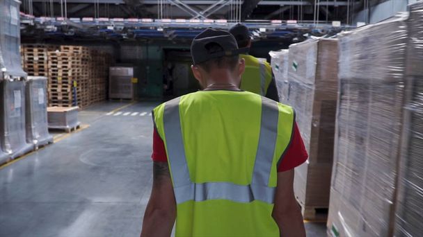 Портрет работника склада в каске и отражающей куртке, идущего между полками склада с коробками. Работник склада
 - Фото, изображение