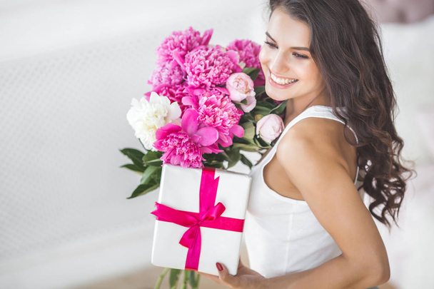 Very beautiful woman with flowers and gift indoors - Photo, Image