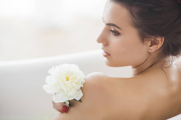 Genç güzel kadın alarak banyo çiçek ve süt ile - Fotoğraf, Görsel