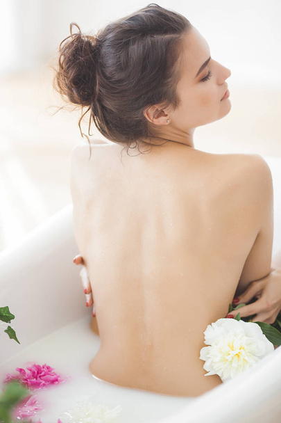 Young beautiful woman taking bath with flowers and milk - Фото, зображення