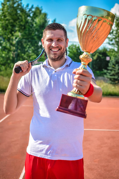 Jugador de tenis masculino feliz con copa y raqueta después del partido
 - Foto, Imagen