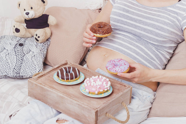 Mulher grávida com diferentes donuts na placa, fundo foco suave
 - Foto, Imagem