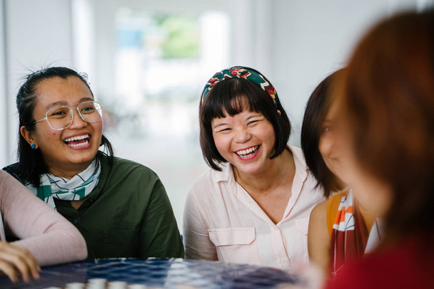 Aasialaiset naiset nauravat ja puhuvat yhdessä pöydässä
 - Valokuva, kuva