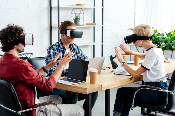 de jeunes collègues qui utilisent des écouteurs et des ordinateurs portables de réalité virtuelle tout en travaillant ensemble
 - Photo, image