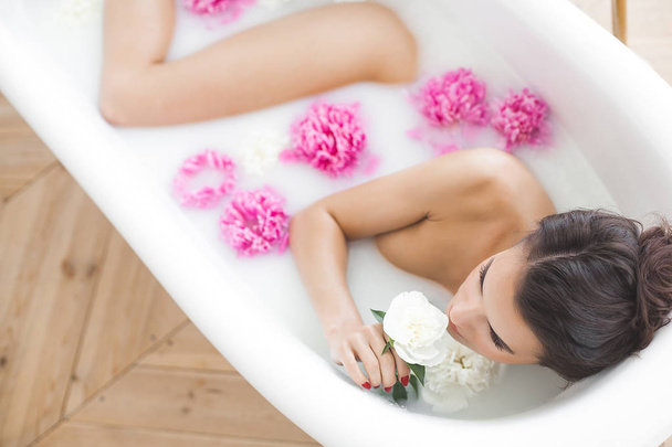 Jovem mulher bonita tomando banho com flores e leite
 - Foto, Imagem