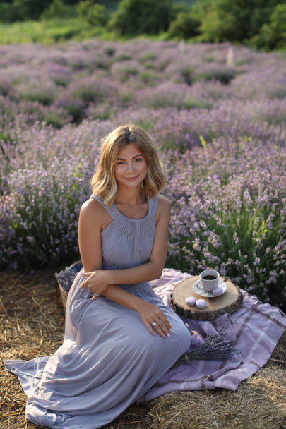 aantrekkelijke vrouw zittend op de deken op picnic in violet lavendel veld  - Foto, afbeelding