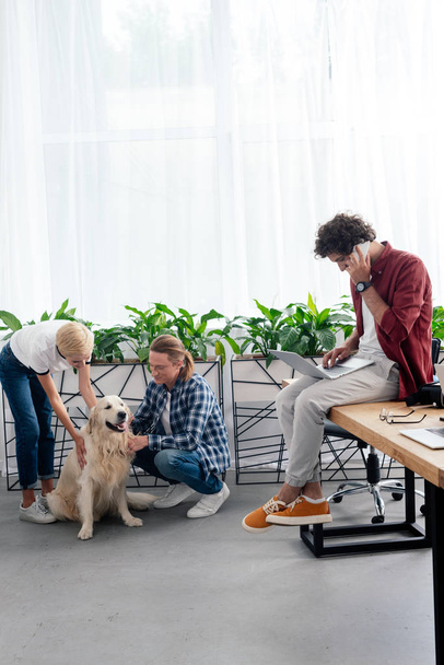 a fiatalember beszél a smartphone, miközben simogatta a kutya az iroda munkatársai - Fotó, kép