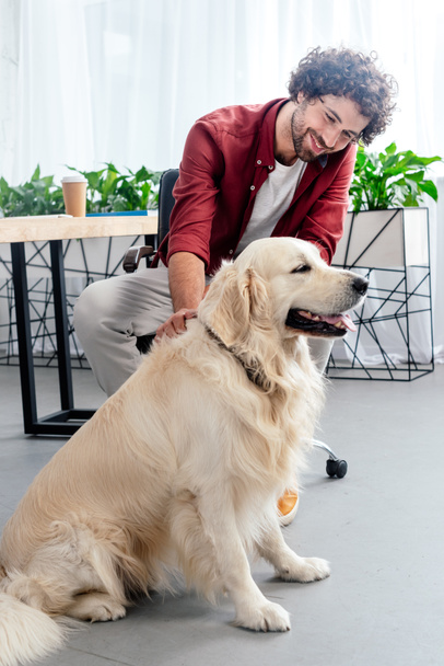 smiling young man stroking dog at workplace - Фото, изображение