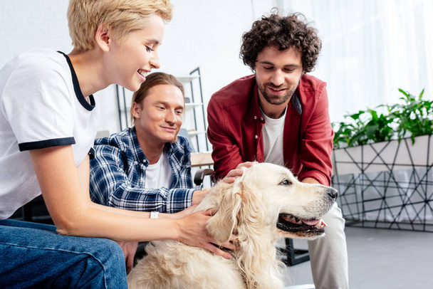 uśmiechający się młodych współpracowników, głaszcząc psa w biurze  - Zdjęcie, obraz