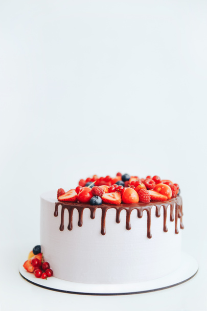 Cake with white cheese cream, decorated with ganache and red berries on a white stand - Photo, Image