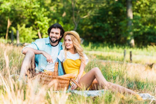 happy couple sitting on blanket at picnic and looking away - Foto, imagen