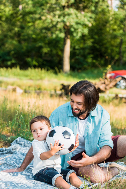happy father and toddler son playing with football ball at picnic - 写真・画像