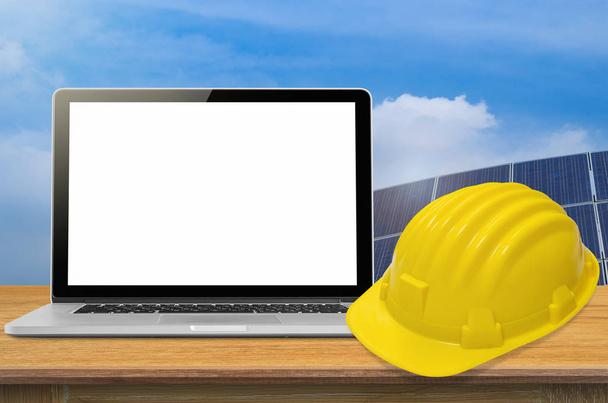 Yellow safety helmet and laptop on desk with industry background, blank on screen. - Photo, Image