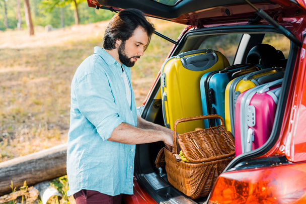 handsome man packing picnic basket at car trunk - Фото, зображення