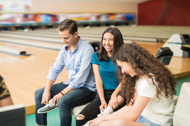 Happy male and female friends wearing shoes before playing bowling in club  - Foto, imagen