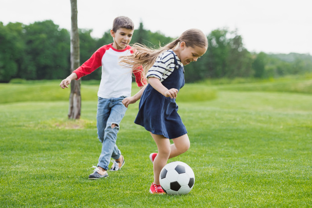 niños pequeños y felices jugando al fútbol en el prado con hierba verde
 - Foto, imagen