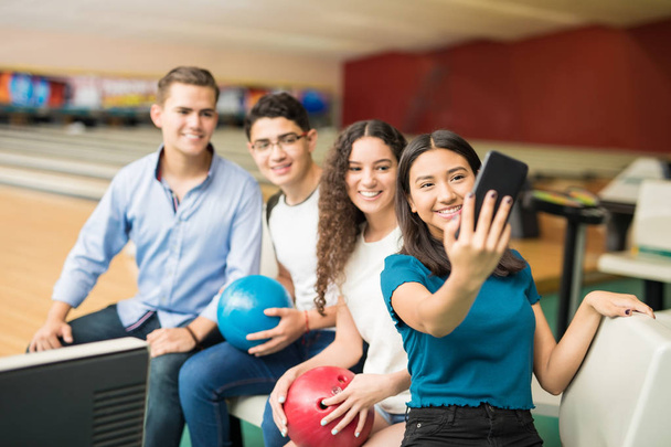 Lachende tienermeisje selfie met vrienden op de mobiele telefoon in bowlingclub - Foto, afbeelding