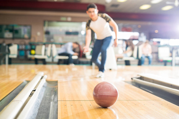 Full length of teenage boy bowling in club with focus on brown ball - Photo, Image