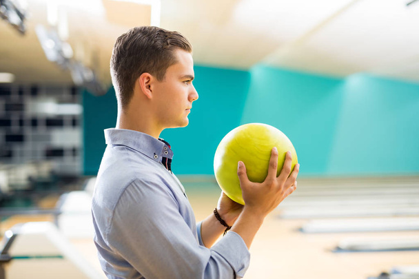 Seitenansicht eines entschlossenen Teenagers, der eine gelbe Bowlingkugel in einer Kegelbahn im Club hält  - Foto, Bild