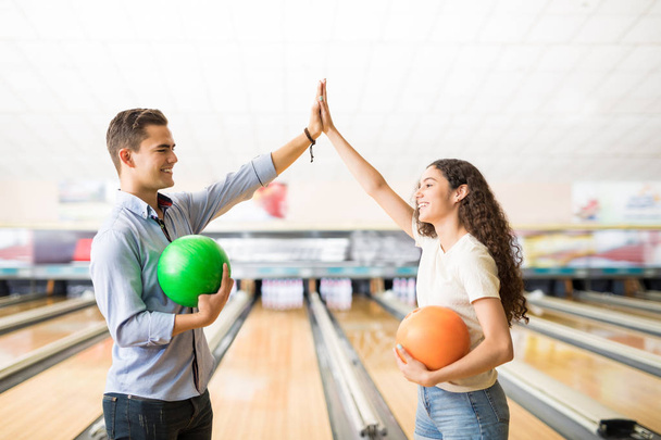 Male and female teenage friends showing team spirit with high-five at bowling alley in club - Фото, изображение