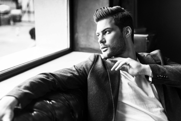 giovane uomo elegante guardando lontano mentre seduto sul divano al negozio di barbiere
 - Foto, immagini