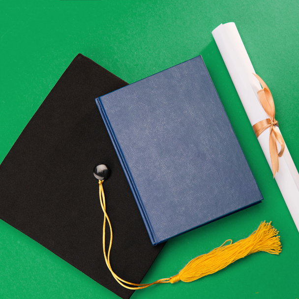 Top view of book, graduation mortarboard and diploma on green - Foto, Imagen