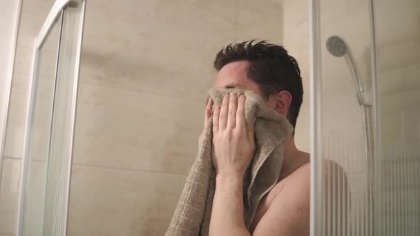 Portret van een jonge man die zijn gezicht met een badhanddoek in de badkamer veegt - Video