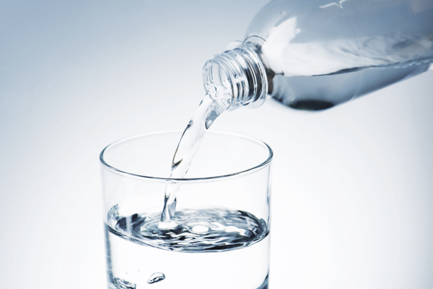 close-up shot of pouring water from plastic bottle into glass - Foto, afbeelding