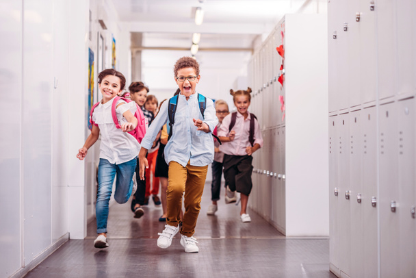 ryhmä ihastuttavia oppilaita juoksemassa koulun käytävällä kameran edessä
 - Valokuva, kuva