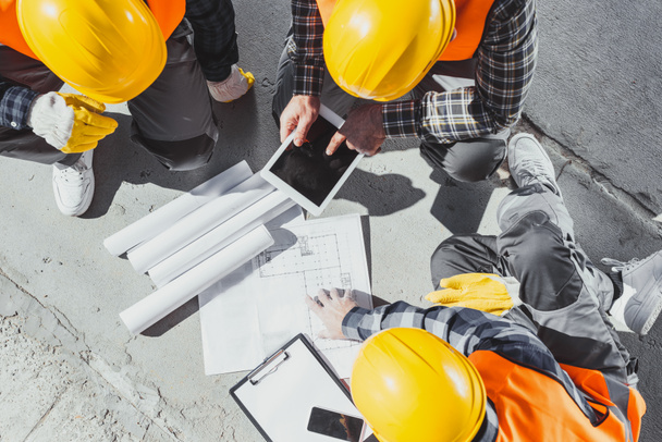 ylhäältä näkymä kolme rakennusalan työntekijää istuu konkreettisia ja keskustella rakennussuunnitelmat
 - Valokuva, kuva