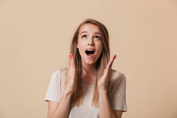 Portrait of a happy casual girl celebrating success with open mouth isolated over beige background - Foto, afbeelding
