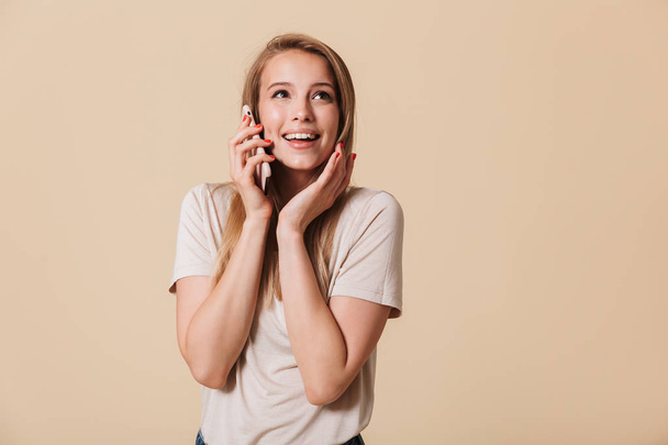 Portrait of a smiling casual girl talking on mobile phone isolated over beige background - Фото, зображення