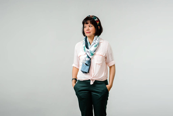 Studio portrait of creative middle aged Chinese Asian woman wearing dark pants and light buttoned shirt with beautiful blue and white scarf - Foto, afbeelding