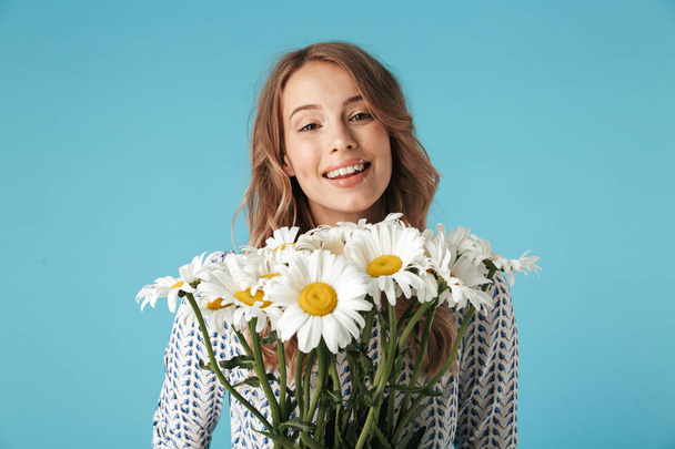 Happy blonde woman in dress holding bouquet of flowers and looking at the camera over blue background - Foto, immagini