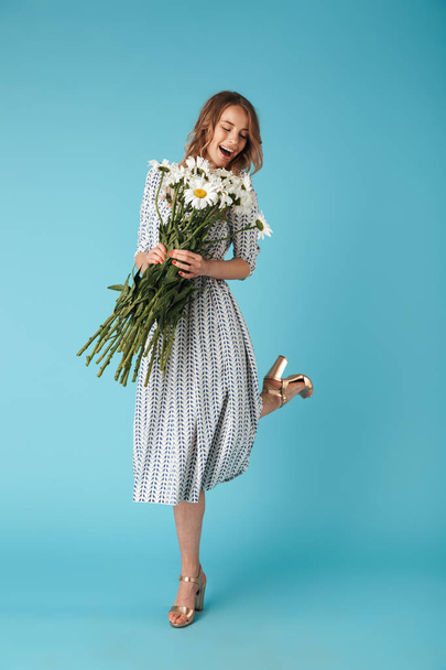 Full length image of Happy blonde woman in dress having fun with flowers over blue background - Photo, Image