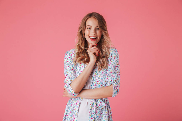 Portrait of a smiling young woman in summer dress looking at camera isolated over pink background - Foto, Imagem