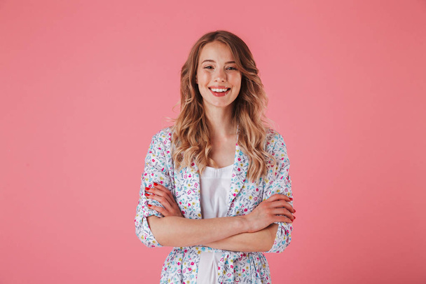 Portrait of a smiling young woman in summer dress looking at camera with arms folded isolated over pink background - Fotografie, Obrázek