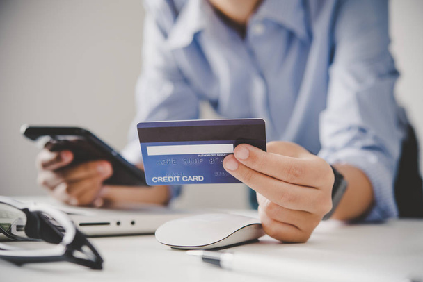 Käsi kädessään luottokortti käsissään ja löytää tietoa tuotteesta käyttäen mobiililaitteella tehdä ostoksia verkossa ja suorittaa rahoitustransaktioita. - Valokuva, kuva