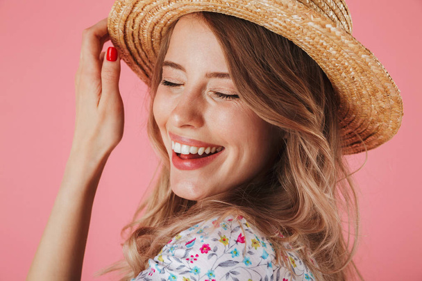 Close up portrait of a laughing young woman in summer dress and straw hat posing isolated over pink background - Φωτογραφία, εικόνα