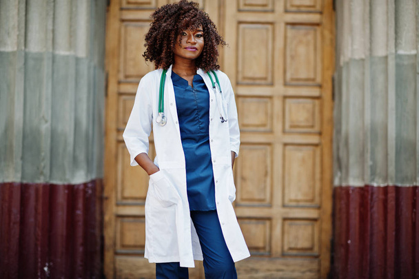 African american doctor female at lab coat with stethoscope outdoor against clinic door. - Fotografie, Obrázek