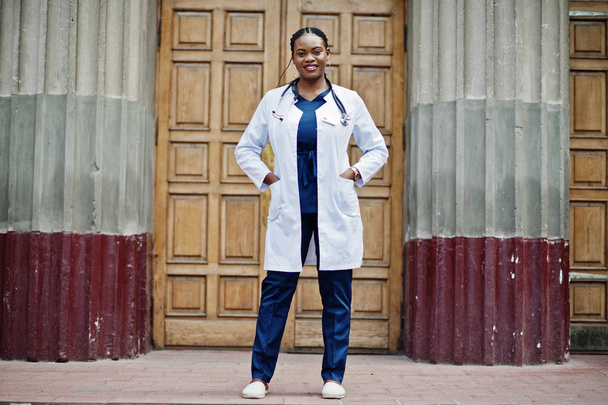 African american doctor female at lab coat with stethoscope outdoor against clinic door. - Фото, зображення