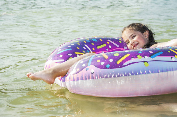 In summer a small smiling girl is floating on the river on a circle. - Foto, imagen