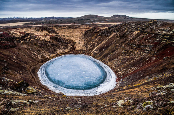Kerid volcanic crater and its blue pond, Golden Circle, Iceland. The winter colours of beautiful Kerio, or Kerid crater in western Iceland. Red volcanic rock, green mossy slopes and a circle of breaking ice in a turquoise lake. - Photo, Image