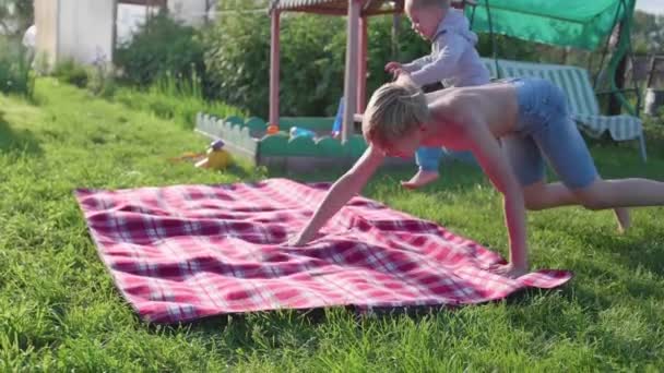 Two children play on the lawn on a hot summer day. Children laugh, they run and fall on the lawn. Outdoor entertainment. Happy childhood - Video, Çekim