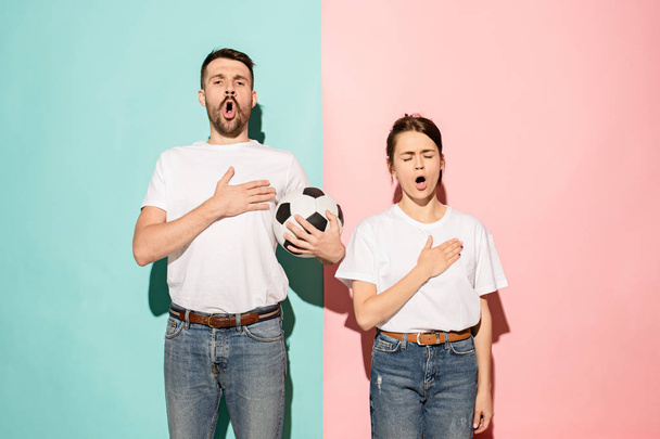 The young fans singing national anthem on blue and pink trendy color studio background. The young man and girl. Fan, football, soccer, support concept. Human emotions concept. - Fotó, kép