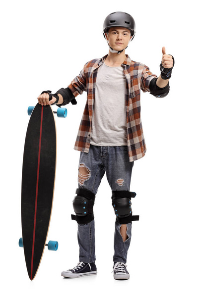 Full length portrait of a teenage skater with protective equipment and a longboard making a thumb up gesture isolated on white background - Photo, Image